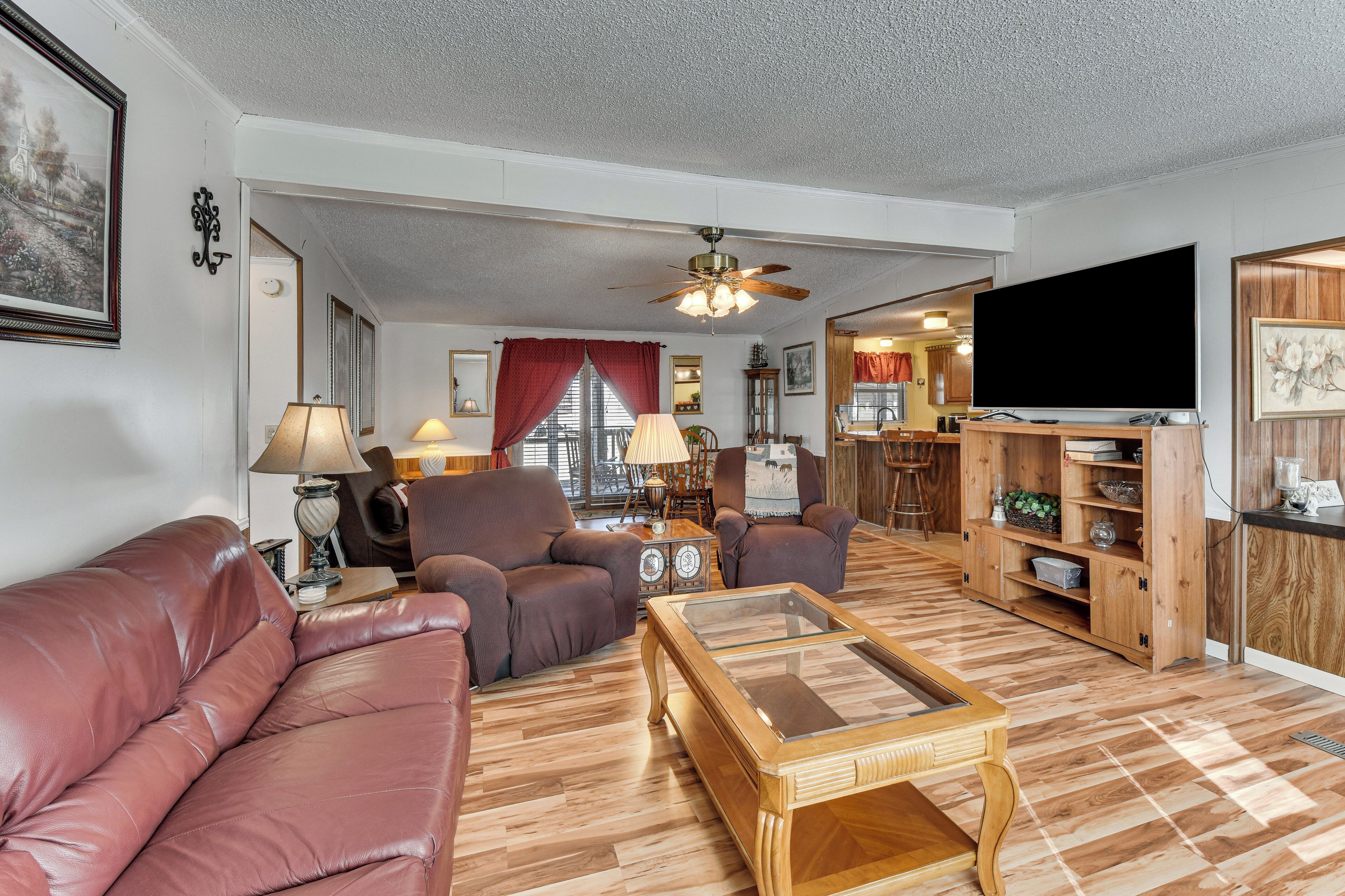 A living room with a leather sofa, two armchairs, a wooden coffee table, a ceiling fan, and a television.