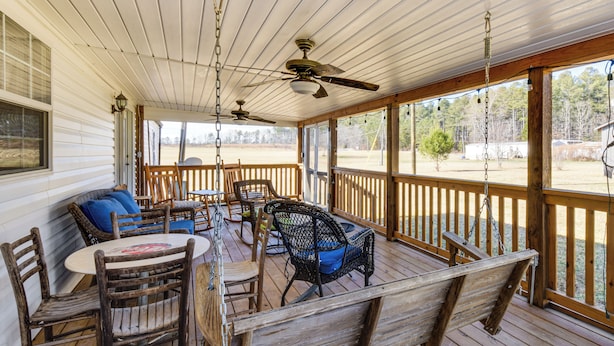 A covered porch with wooden furniture, including chairs and a table, and ceiling fans. - Countryside Haven w/ Spacious Yard in Tamassee! (Tamassee)