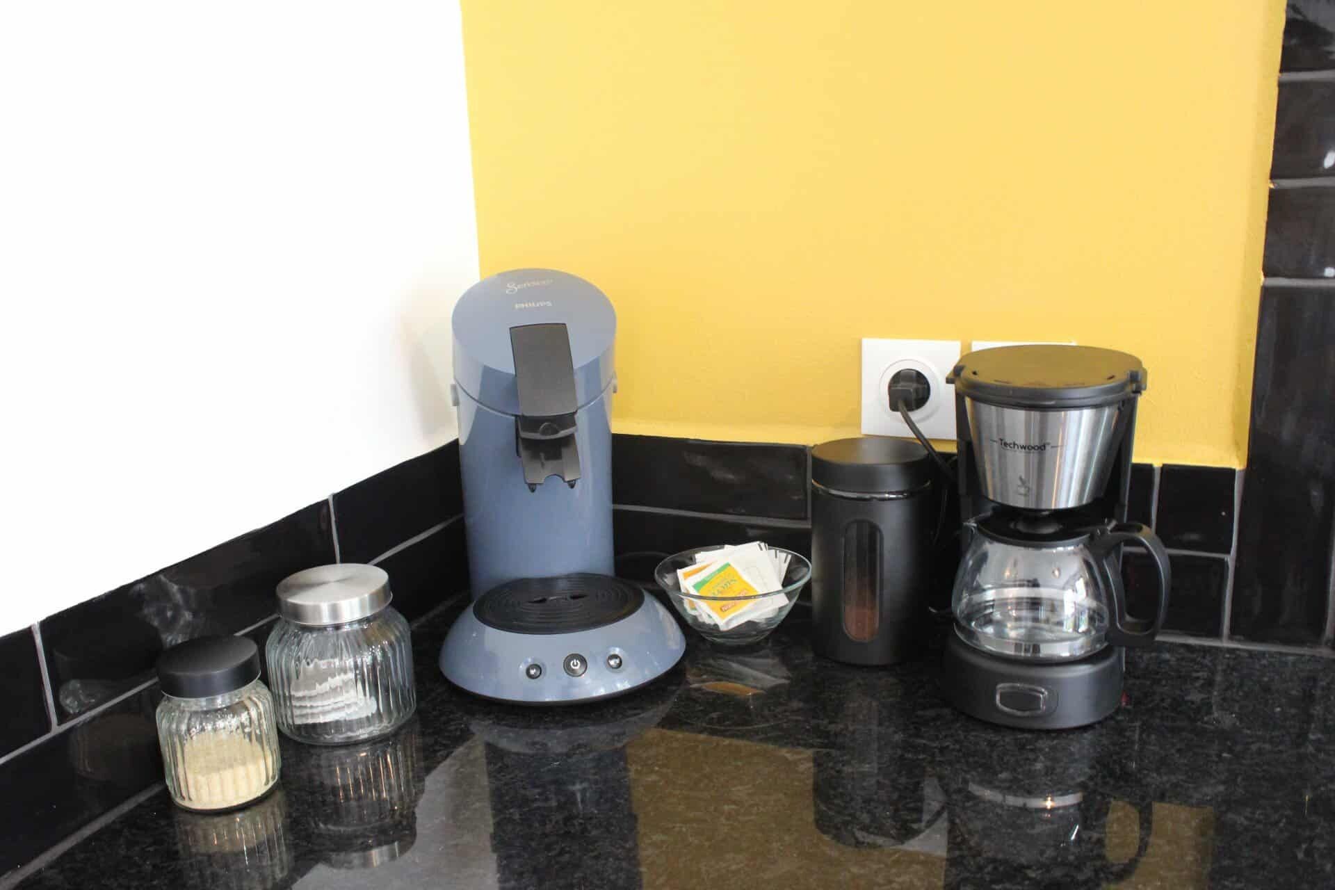 Una encimera de cocina con cafetera, licuadora y jarra para café.