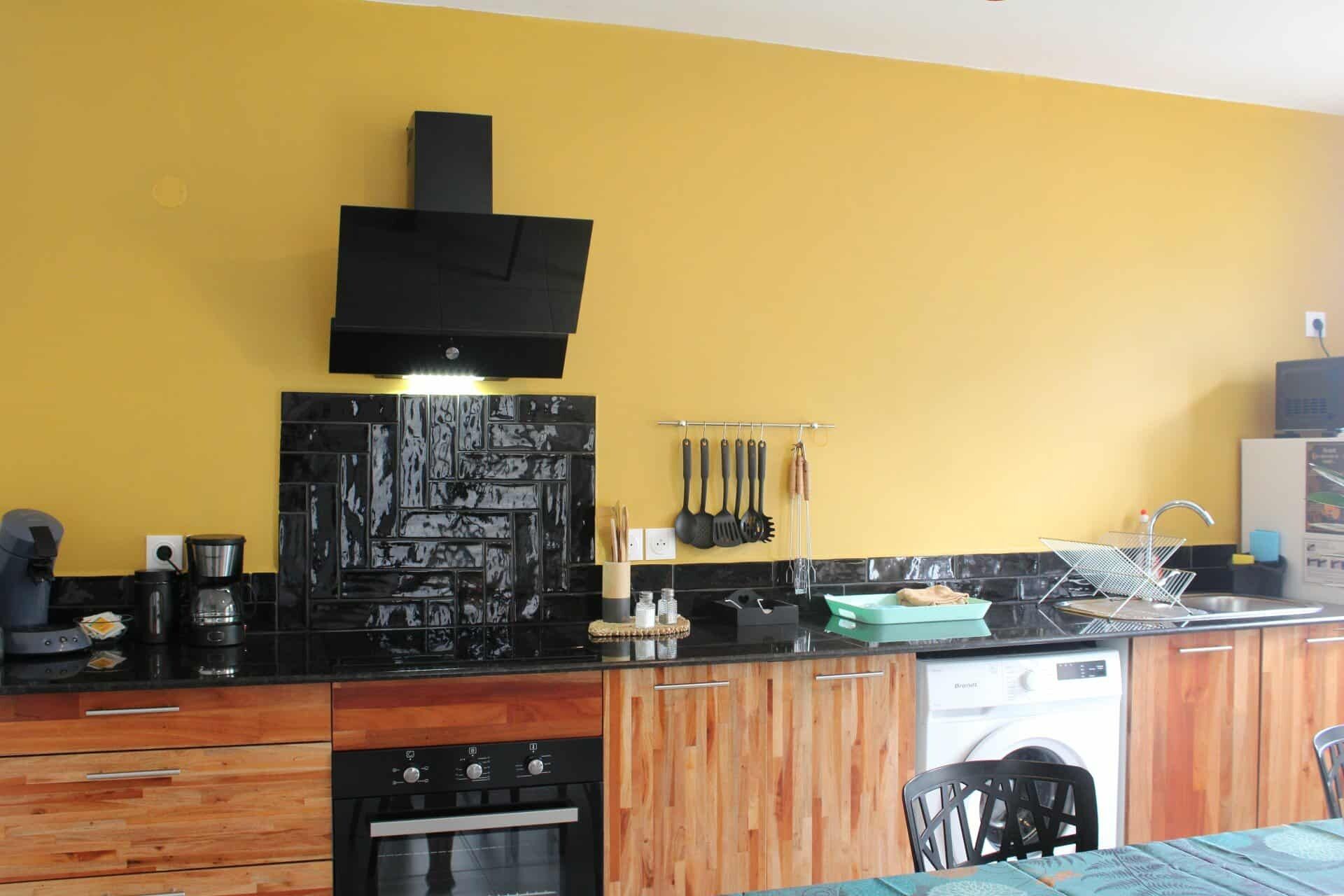 Une cuisine avec des meubles de rangement en bois, un plan de travail noir, un four encastré et un four à micro-ondes.