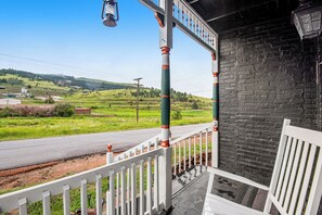 A porch with a white railing, a bench, and a view of a green landscape with a road and hills in the background. - 4BR Mountain-view Home - Deck, Washer & Dryer (Cripple Creek)