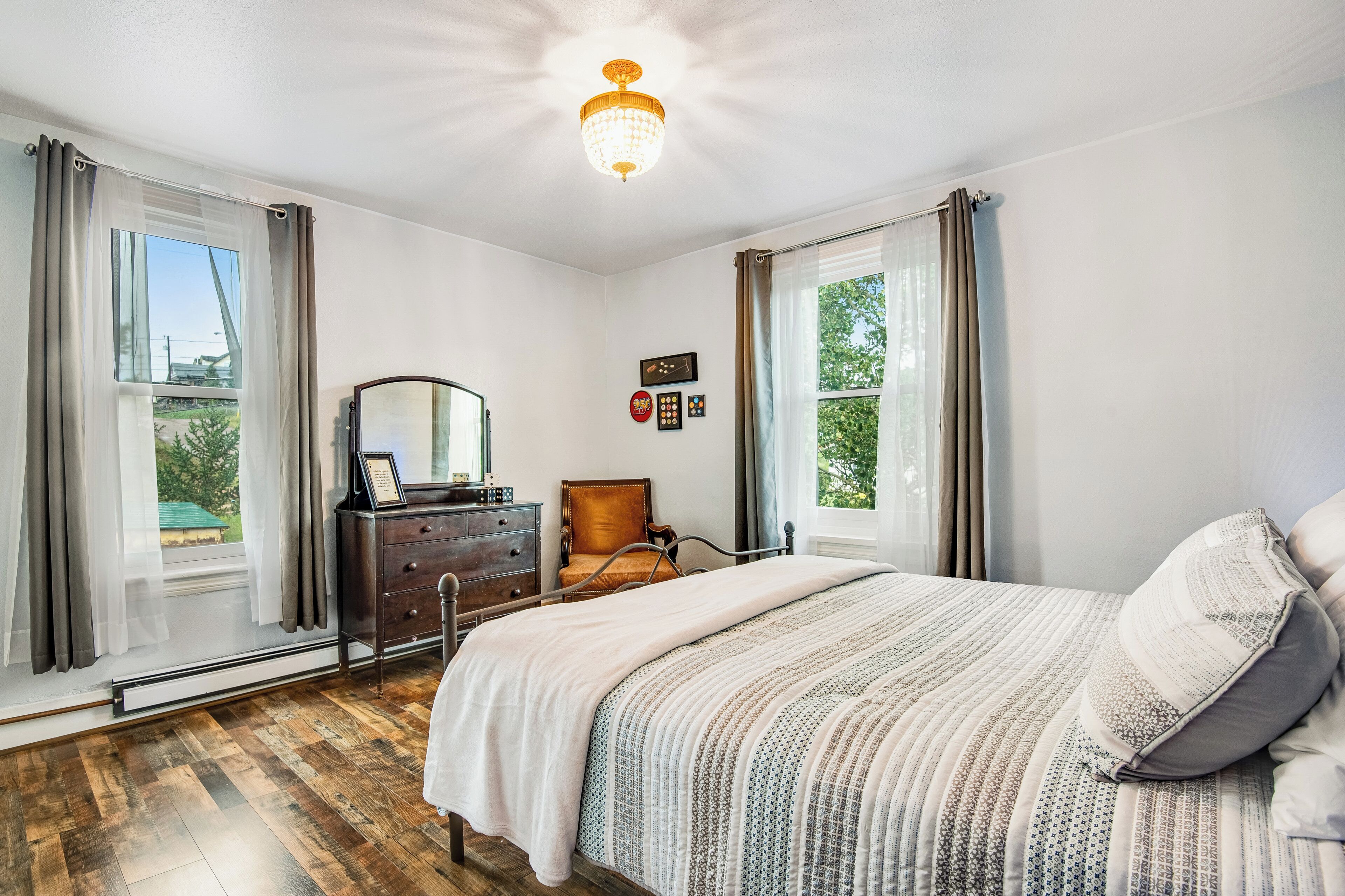 Une chambre à coucher avec un grand lit, une commode, une chaise et une fenêtre avec des rideaux.