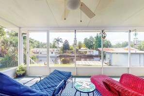 A room with a large window, a ceiling fan, a blue and red sofa, and a small table with a decorative item. - Sunshine House Directly on a Canal (Astor)