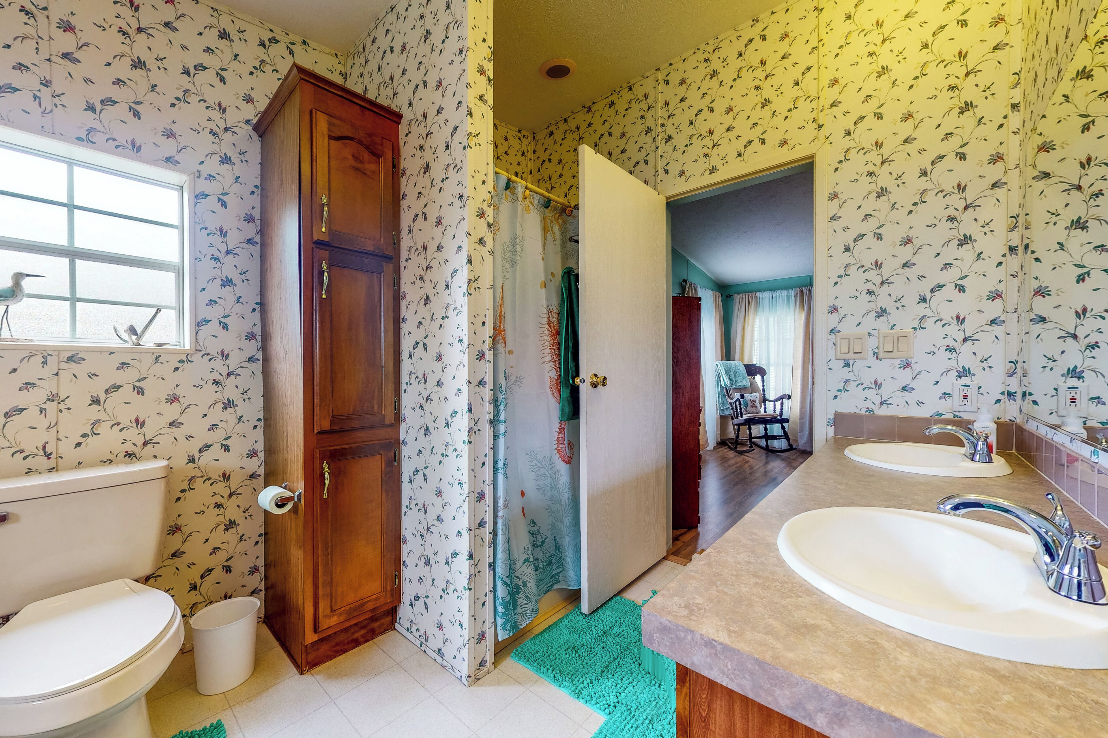 Ein Badezimmer mit floralem Wandpapier, einem Holzkästen, einer Toilette und einem Waschbecken mit Spiegel.