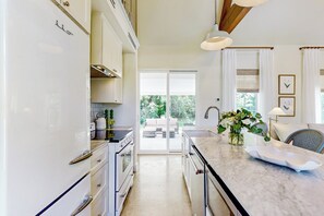 A modern kitchen with white cabinets, a marble countertop, and a view to an outdoor seating area. - Eco-chic Lake Somerville Area Farmhouse w/ Porch (Brenham)