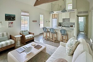 A spacious living room with a sofa, chairs, and a coffee table. A kitchen with bar stools and a dining area is visible in the background. - Eco-chic Lake Somerville Area Farmhouse w/ Porch (Brenham)