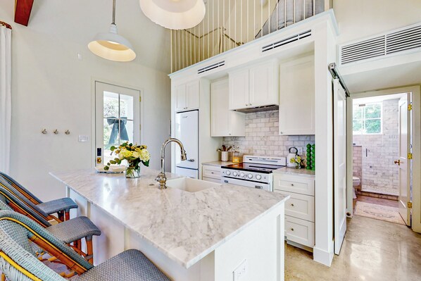 A modern kitchen with white cabinets, a marble island, and a built-in oven. - Eco-chic Lake Somerville Area Farmhouse w/ Porch (Brenham)