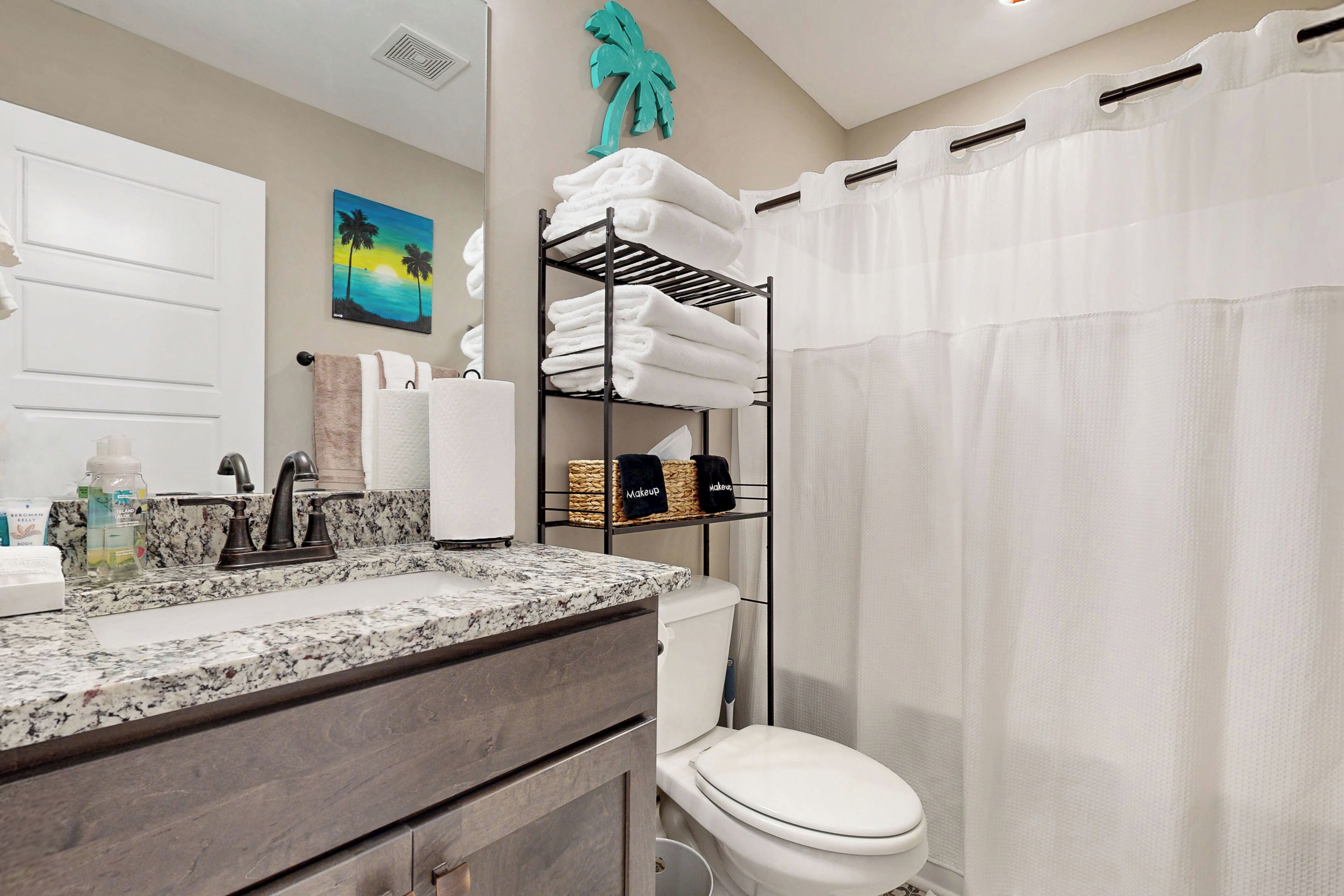 A bathroom with a marble countertop, a white toilet, a shelf with folded towels, and a teal palm tree decoration.