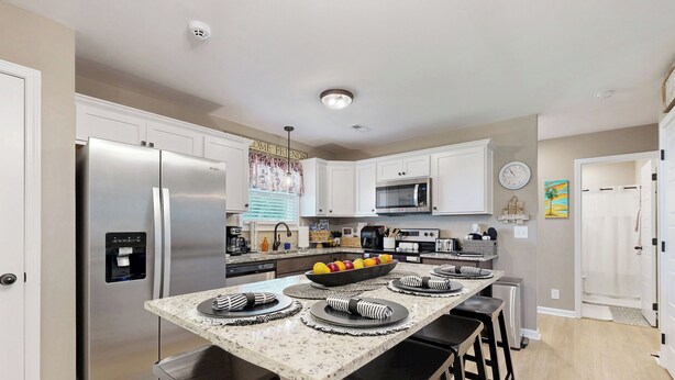 A modern kitchen with white cabinets, stainless steel appliances, a central island with stools, and a fruit bowl. - Gateway to Fort Campbell! Home w/ Furnished Deck (Clarksville)