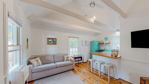Ein modernes Wohnzimmer mit grauem Sofa, Holzboden und einer Küchenzeile mit turquoise Arbeitsplatte und weißen Barhocker.