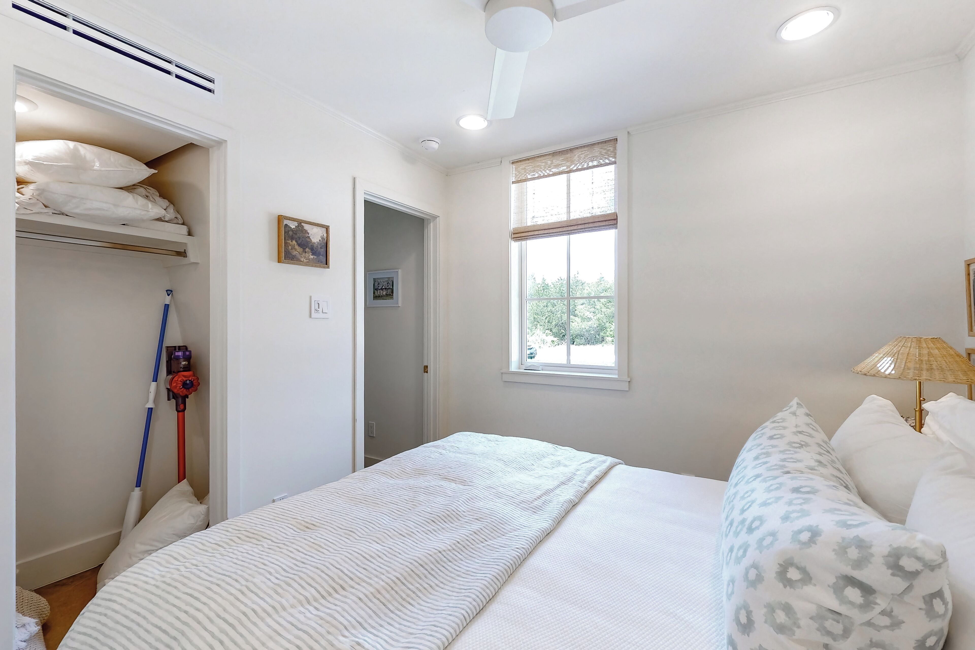 A bedroom with a bed, a window with a view, a ceiling fan, and a wall-mounted heater.