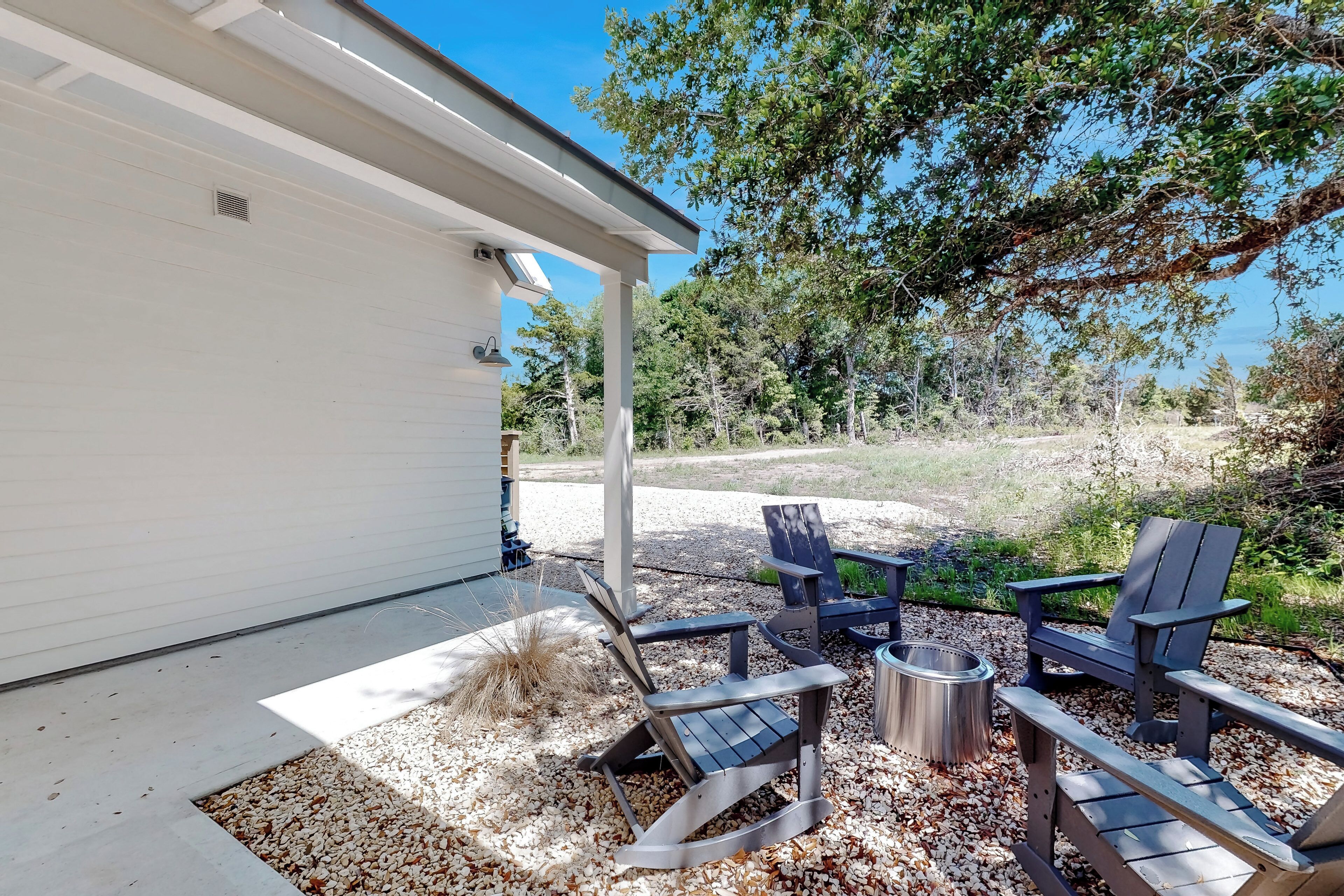 A patio area with Adirondack chairs, a fire pit, and a white building.