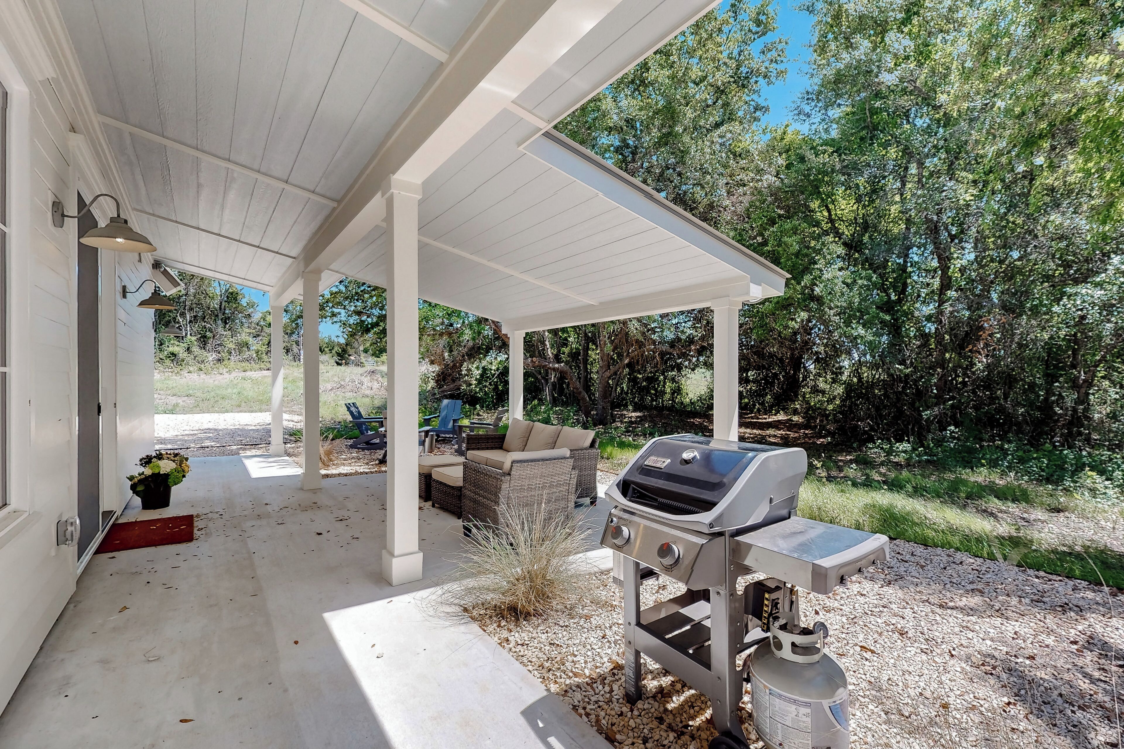 Un patio techado con una parrilla, mobiliario exterior y vistas a los árboles circundantes.