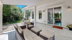 Egy fedett terasz, amelyen fonott bútorok, egy grillező és a kertre néző kilátás található.