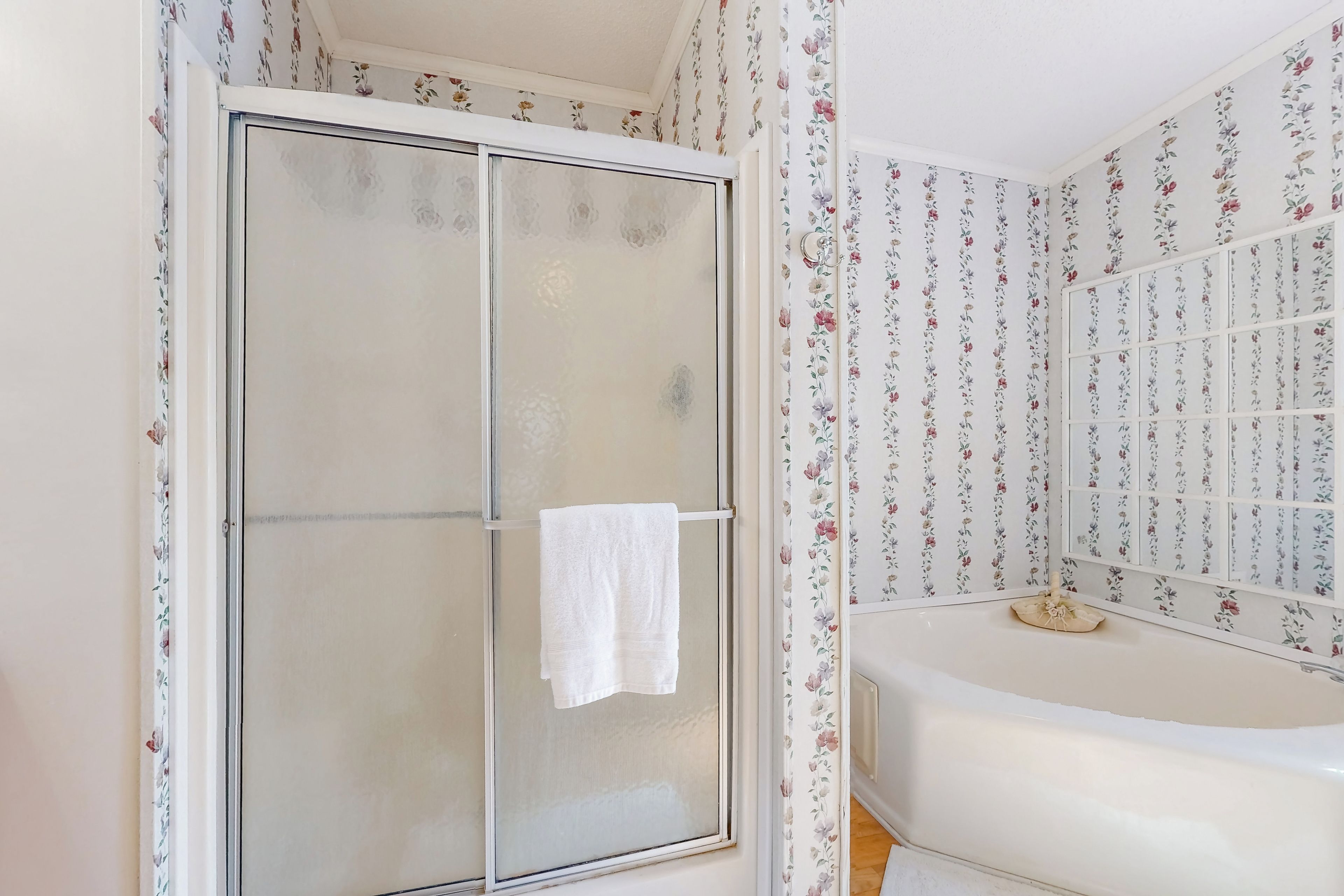 Ein Badezimmer mit Duschabtrennung aus Glas, einer weißen Badewanne und blumigem Wandpapier.