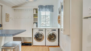 A laundry area with two front-loading washing machines, a bench, a trash bin, and a window with a view of trees. - 12 Mi to Bromley Mtn Ski Resort: Quiet Hideaway (Manchester Center)