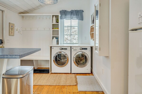 A laundry area with two front-loading washing machines, a bench, a trash bin, and a window with a view of trees. - 12 Mi to Bromley Mtn Ski Resort: Quiet Hideaway (Manchester Center)