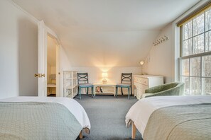 Quarto com duas camas, uma escrivaninha, cadeiras, cômoda e uma janela.