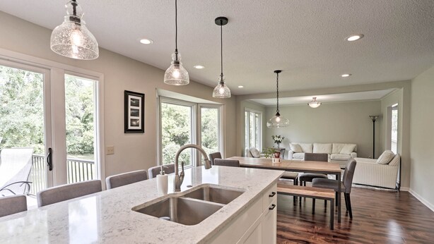 A spacious kitchen with a large island, a dining area with a wooden table and chairs, and a living area with a sofa and a coffee table. - Plymouth House: Walk to Beach & Medicine Lake! (Plymouth)