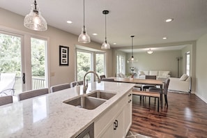 A spacious kitchen with a large island, a dining area with a wooden table and chairs, and a living area with a sofa and a coffee table. - Plymouth House: Walk to Beach & Medicine Lake! (Plymouth)
