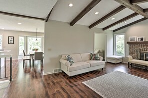 A spacious living room with hardwood floors, a white sofa with patterned cushions, a fireplace, and a dining area with a table and chairs. - Plymouth House: Walk to Beach & Medicine Lake! (Plymouth)