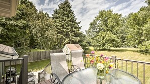 A glass-top table with chairs on a deck, overlooking a backyard with a wooden fence and trees. - Plymouth House: Walk to Beach & Medicine Lake! (Plymouth)