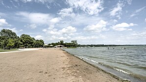 A sandy beach with a calm lake, trees, and a few people swimming. - Plymouth House: Walk to Beach & Medicine Lake! (Plymouth)