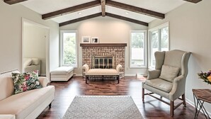 A spacious living room with a fireplace, a high ceiling with exposed beams, a comfortable armchair, and a sofa. - Plymouth House: Walk to Beach & Medicine Lake! (Plymouth)