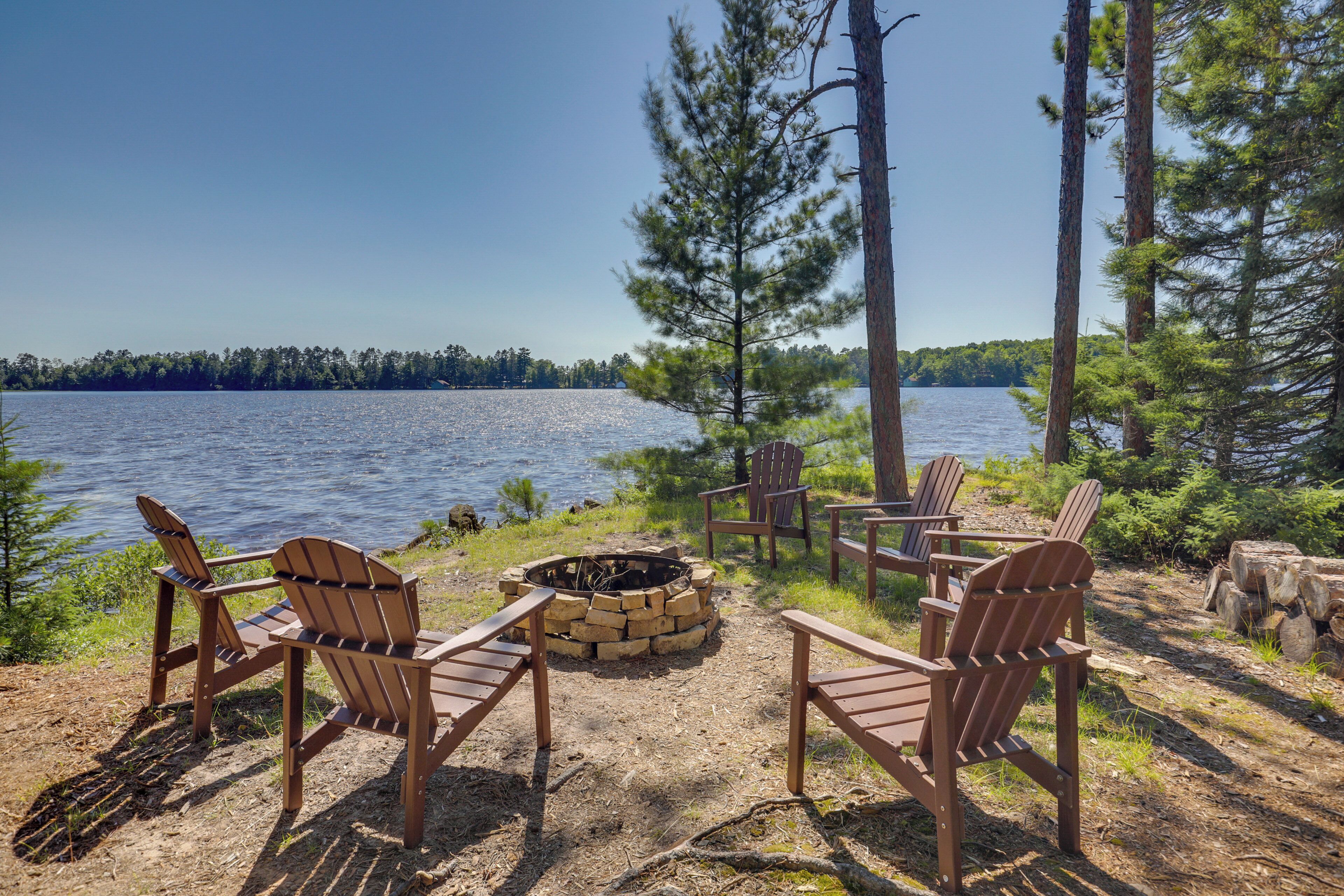 Kaunis paikka järven rannalla, jossa on puusta valmistettuja Adirondack-tyylisiä tuoleja aseteltuna nuotiopaikan ympärille. Alue on metsän ympäröimä, ja sieltä on esteetön näkymä järvelle.