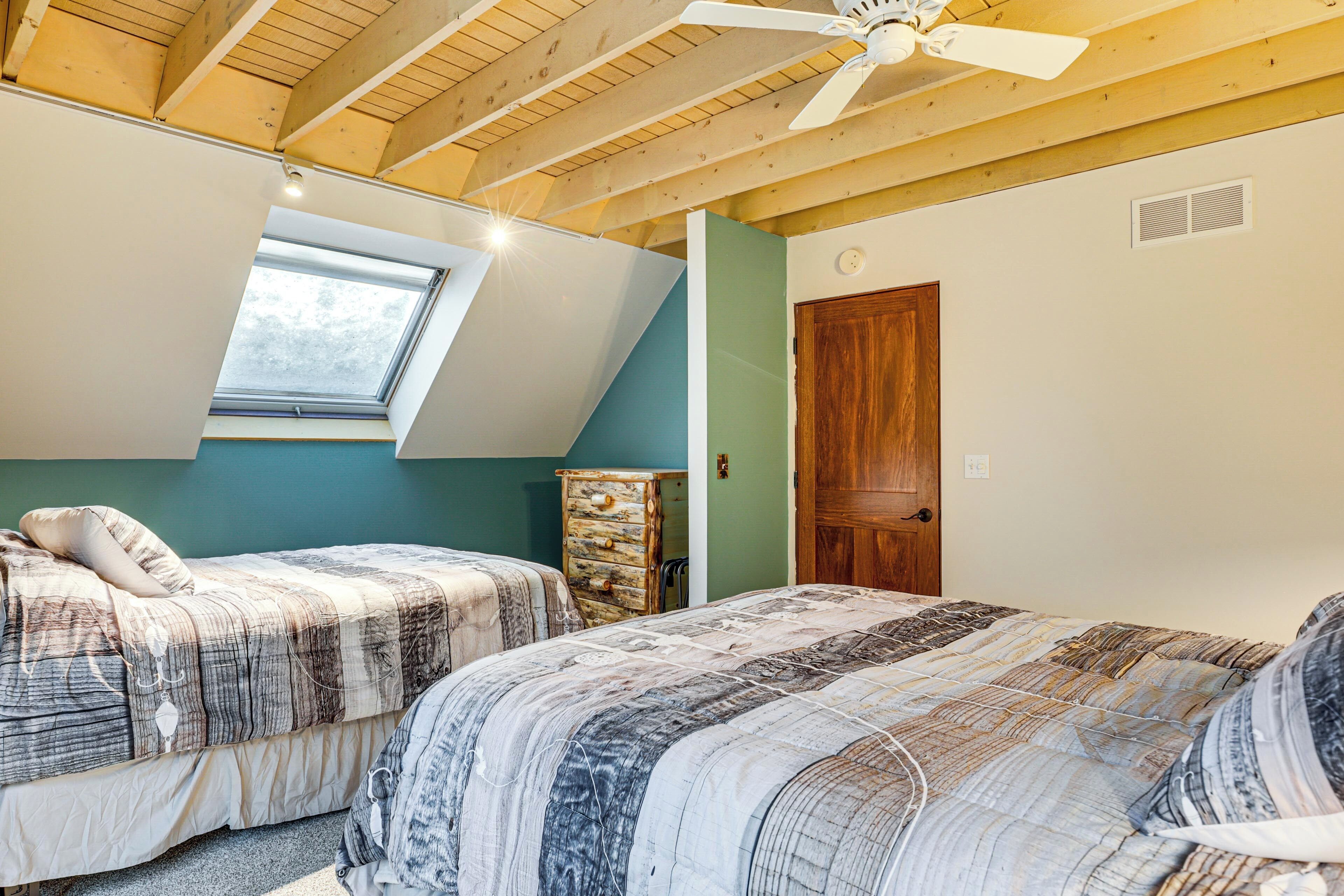 A bedroom with two beds, a skylight, a ceiling fan, and a wooden door.