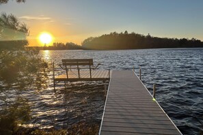 A wooden dock extending into calm water with a bench at the end, surrounded by trees and a clear sky. - Private Peninsula! Laurel Lake Retreat w/ 3 Piers (Three Lakes)
