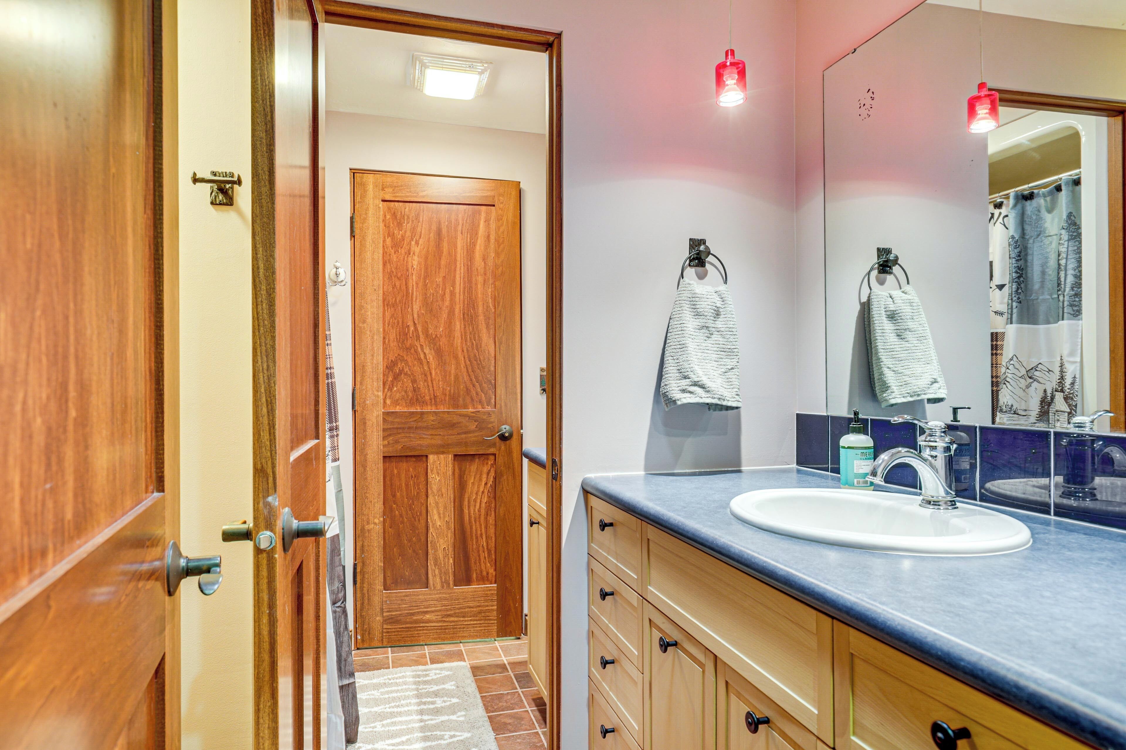 Une salle de bain avec une porte en bois, un lavabo avec un miroir et des serviettes suspendues à des crochets.