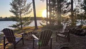 Δύο ξύλινες πολυθρόνες Adirondack τοποθετημένες δίπλα σε μια λίμνη, με θέα το ηλιοβασίλεμα.