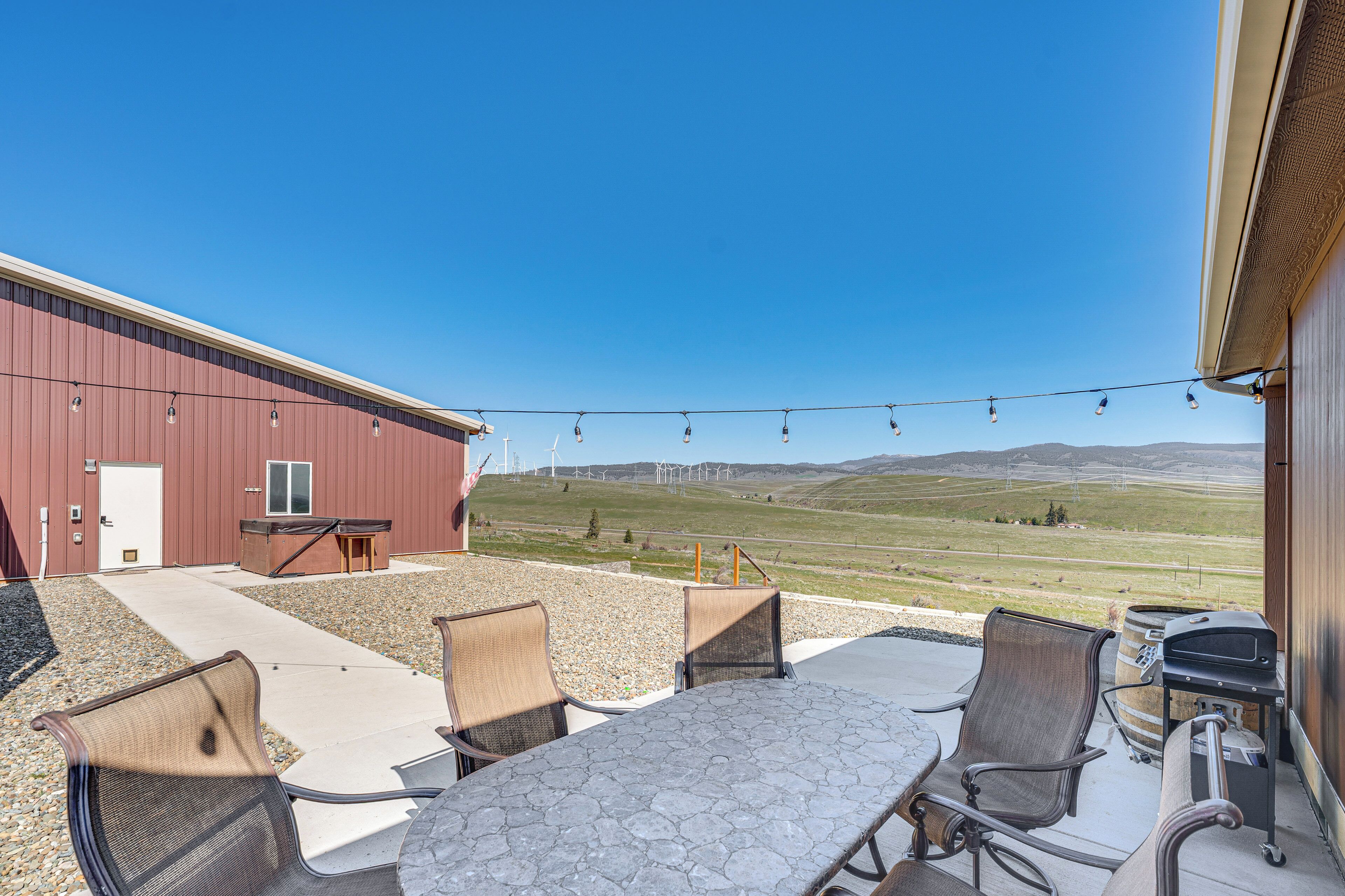 An outdoor patio with a table and chairs, a barbecue grill, and a view of wind turbines in the distance.