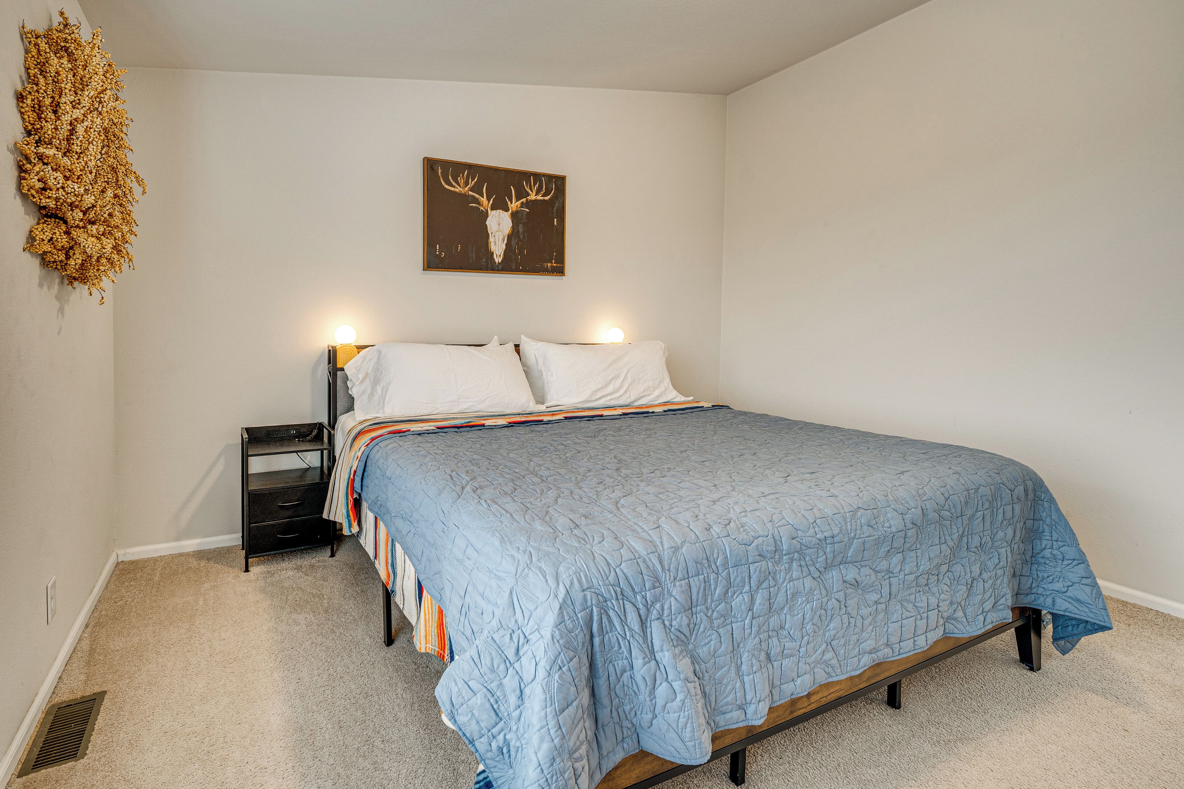 Une chambre à coucher comprenant un lit, une table de chevet, une lampe fixée au mur et une œuvre d’art représentant un crâne de cerf.