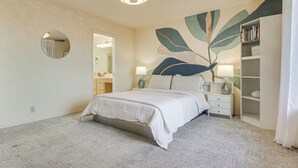 Ein Schlafzimmer mit Bett, Nachttischen, einem Spiegel, einem Bücherregal und einer Deckenleuchte.