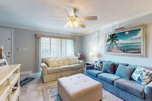 A living room with a beige sofa, a blue sofa, a ceiling fan, a painting of a beach, and a wooden floor. - 1 Mi to Beach! Marco Island Family Getaway w/ Pool (Marco Island)