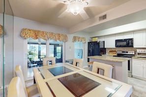 A modern kitchen with white cabinets, a microwave, a stove, and a dining area with a glass table and chairs. - 1 Mi to Beach! Marco Island Family Getaway w/ Pool (Marco Island)