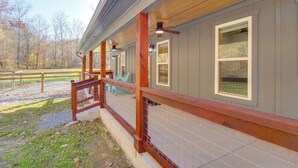 A covered outdoor area with a wooden railing, a tiled floor, and a view of a forested area. - Lyles Cottage: Couple's Retreat w/ Covered Porch (Lyles)