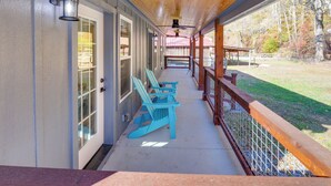 A covered porch with blue Adirondack chairs, a wooden ceiling, and a view of a grassy yard with trees. - Lyles Cottage: Couple's Retreat w/ Covered Porch (Lyles)