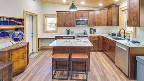 A modern kitchen with wooden cabinets, a central island with stools, a microwave, and a sink. - Lyles Cottage: Couple's Retreat w/ Covered Porch (Lyles)