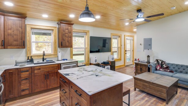 A spacious kitchen with wooden cabinets, a marble island, and a ceiling fan. - Lyles Cottage: Couple's Retreat w/ Covered Porch (Lyles)