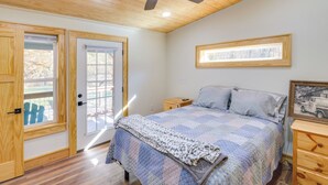 A bedroom with a wooden ceiling, a ceiling fan, a bed with a patterned quilt, a nightstand, and a framed picture on the wall. - Lyles Cottage: Couple's Retreat w/ Covered Porch (Lyles)