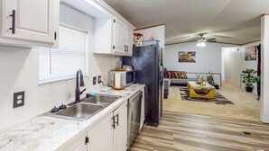 A compact kitchen with a sink, microwave, and refrigerator. There is a dining area with a sofa and a coffee table. The room has a ceiling fan and a window with blinds. - Private Pool! Nat'l Forest Retreat on 1 Acre (Oakhurst)