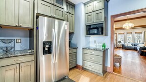A kitchen with a stainless steel refrigerator, wooden cabinets, a microwave, and a dining area with a black leather couch. - Private Hot Tub & Patio! Chicagoland Extended Stay (Lansing)