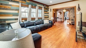 A modern living room with a black leather sofa, a glass coffee table, and a wooden floor. - Private Hot Tub & Patio! Chicagoland Extended Stay (Lansing)