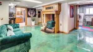 A spacious living room with a green sofa, a fireplace, and a kitchen area visible through an open door. - Private Hot Tub & Patio! Chicagoland Extended Stay (Lansing)