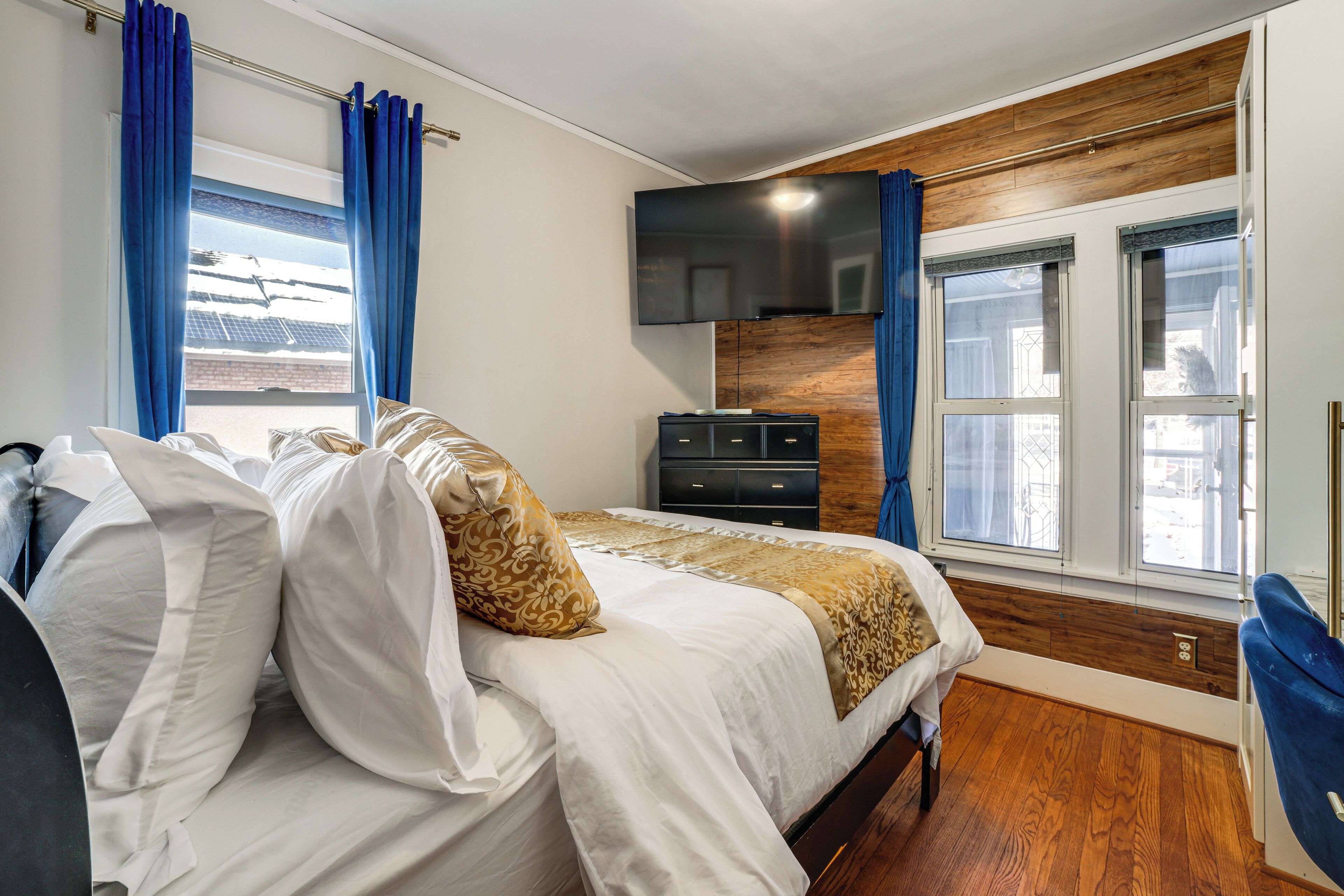 Un dormitorio con cama, televisor, cómoda y ventana con cortinas.