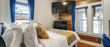 Un dormitorio con cama, televisor, cómoda y ventana con cortinas.