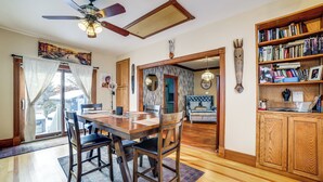 A dining area with a wooden table and chairs, a ceiling fan, and a bookshelf with books and decorative items. - Private Hot Tub & Patio! Chicagoland Extended Stay (Lansing)